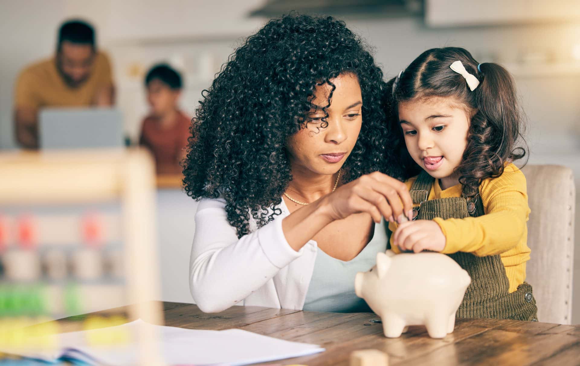Woman, child with piggy bank and man and child in background