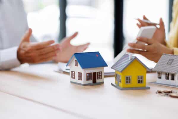 Two small wooden houses on a table next to hands