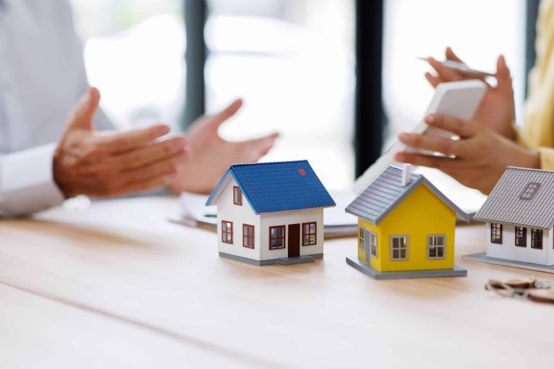 Two small wooden houses on a table next to hands