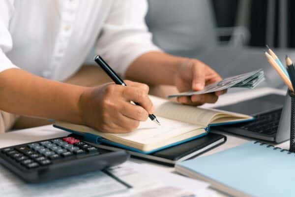Hands holding a pen and paper writing something down next to a calculator and documents