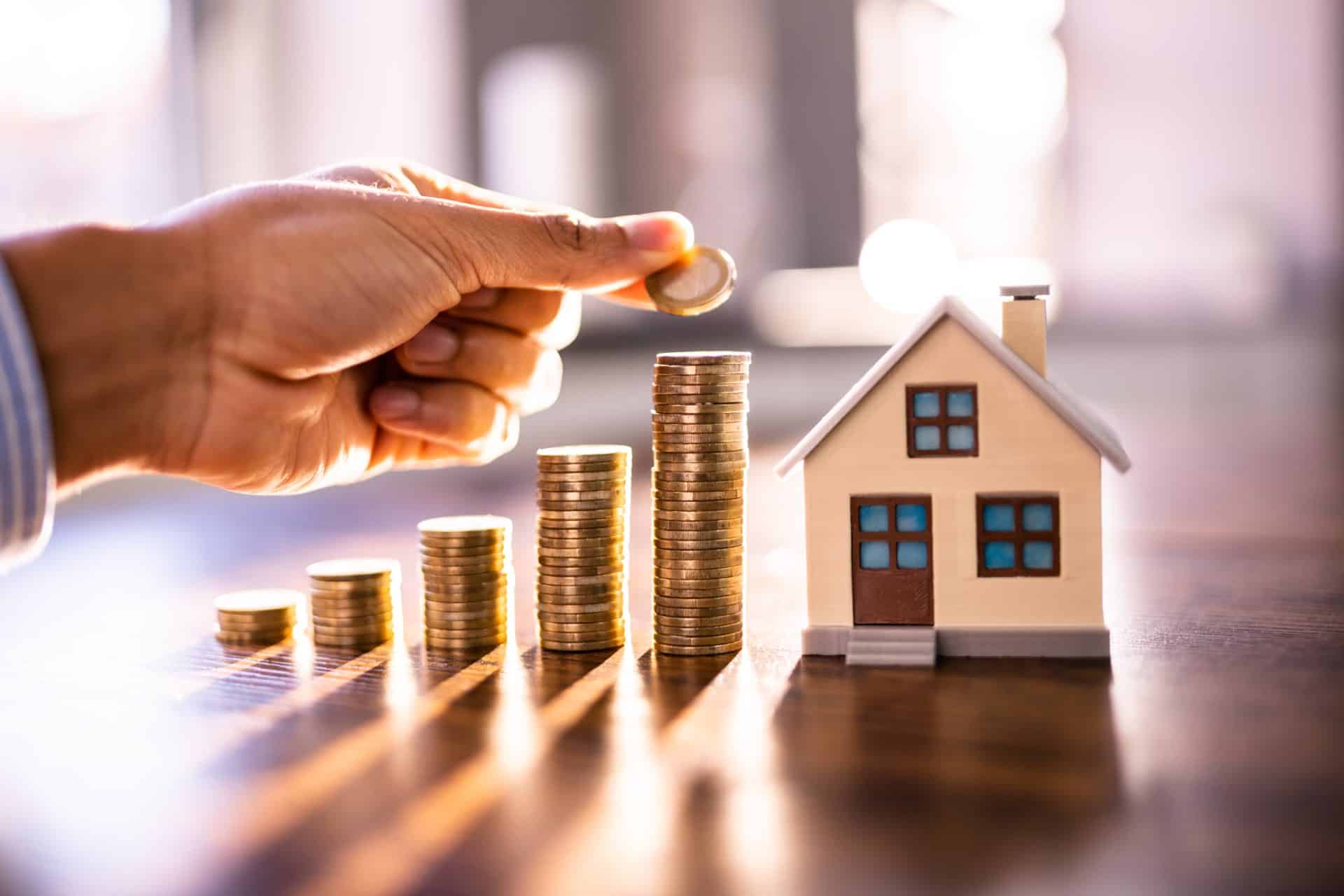 A hand putting change into stacks next to a little wooden house