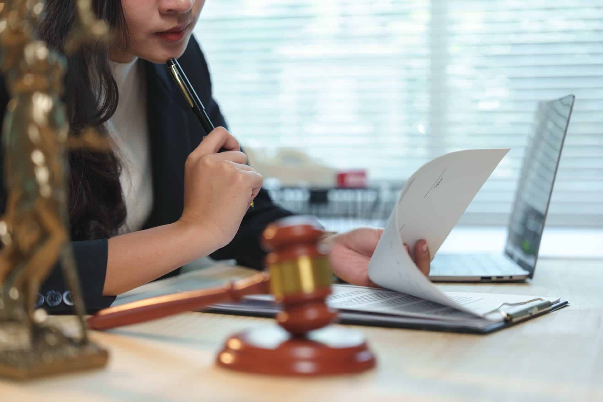 Female lawyer carefully reviewing paperwork next to a gavel and laptop