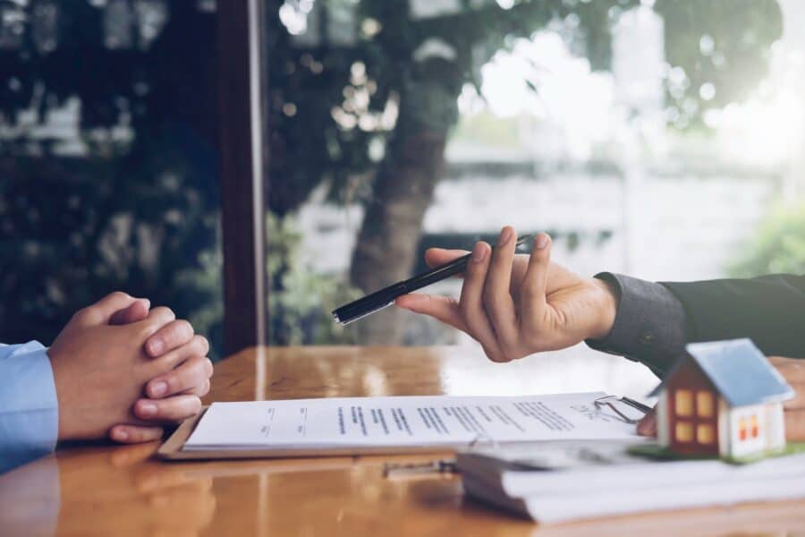 A hand holding a pen next to a clipboard and papers